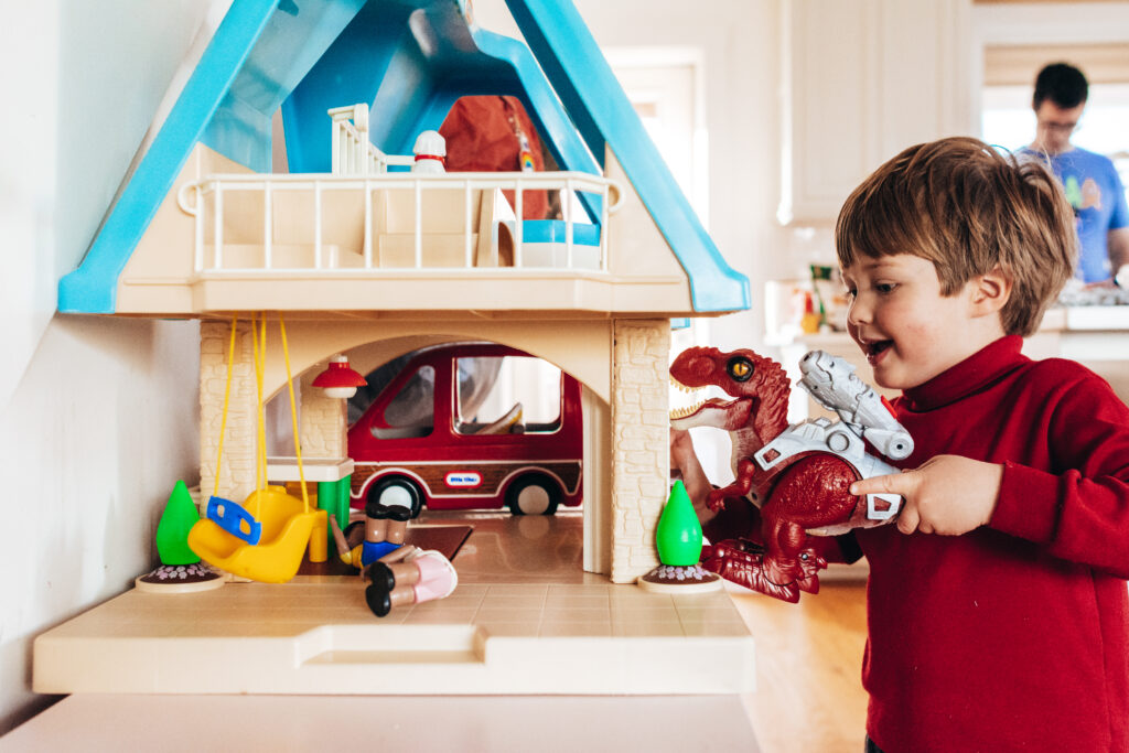 toddler boy and girl playing with red dinosaur in a dollhouse
