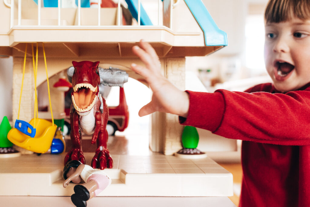 Toddler boy playing with a red dinosaur in a doll house