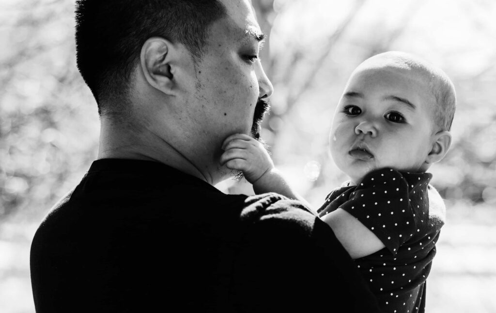A dad holds his crying baby as the baby touches his face outside on their patio in Fairfax VA during a family photo session
