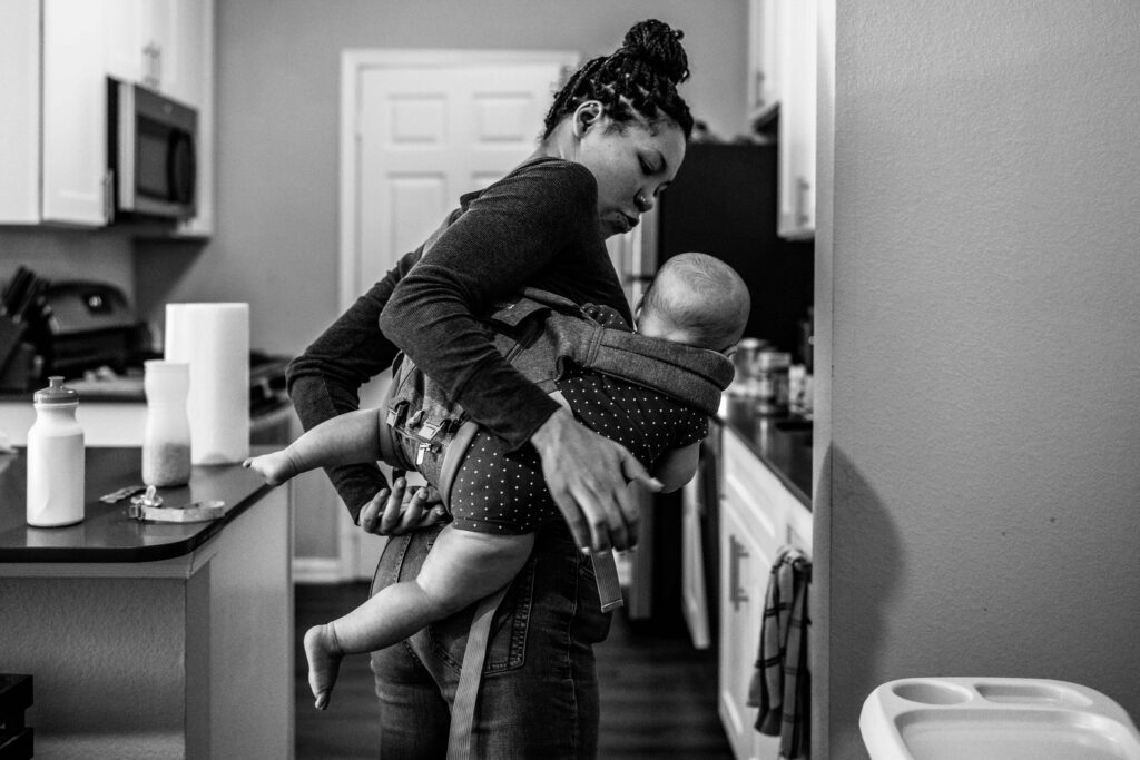 A mom is taking her baby out of a baby carrier in her kitchen so she can put it in the high chair for a snack during a documentary family photo session in Fairfax VA