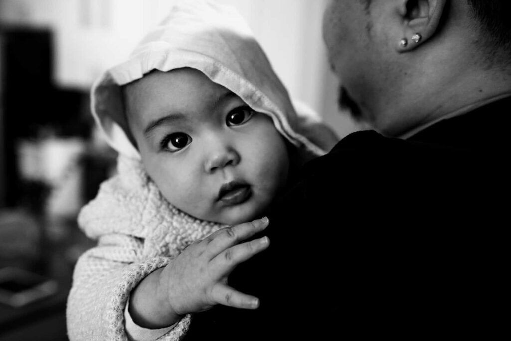 A baby looks at the camera while her dad holds her during a documentary family photography session by These Days Photography in Fairfax, VA