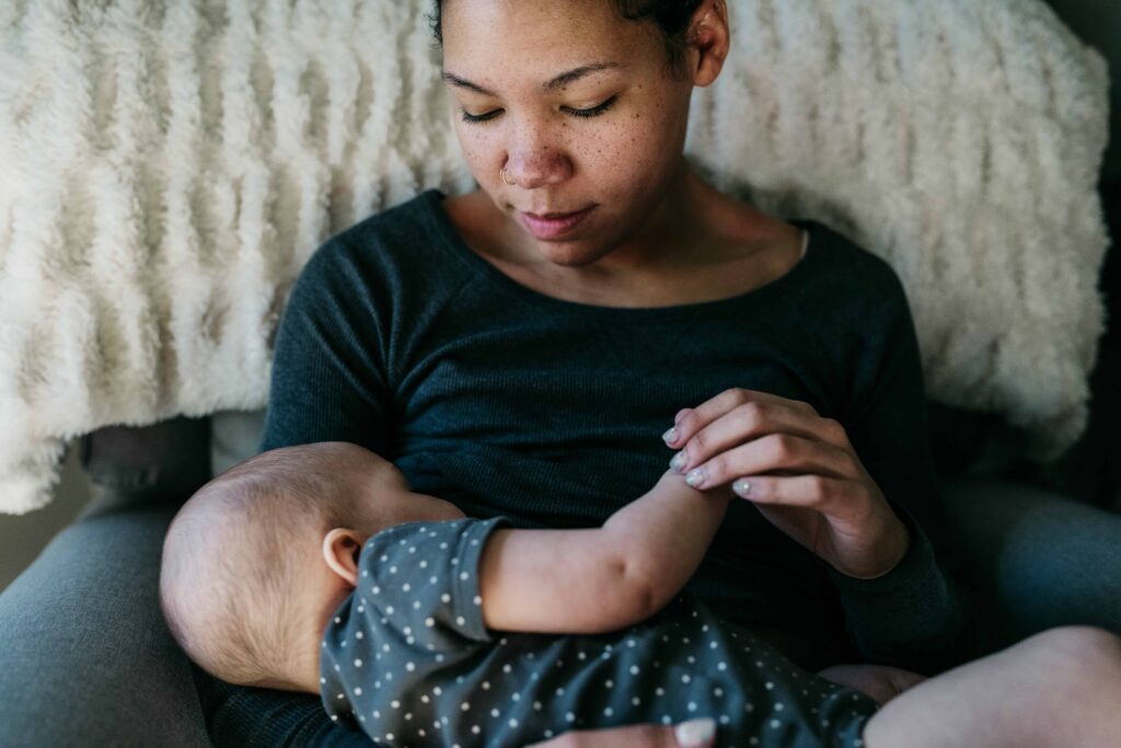 A mother breastfeeds her infant while gazing at her and holding the baby's hand