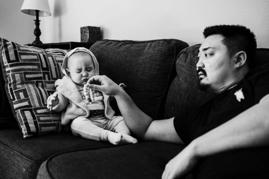A dad plays with his baby on the couch while the baby sneezes during an in-home family photography session in Fairfax, VA

